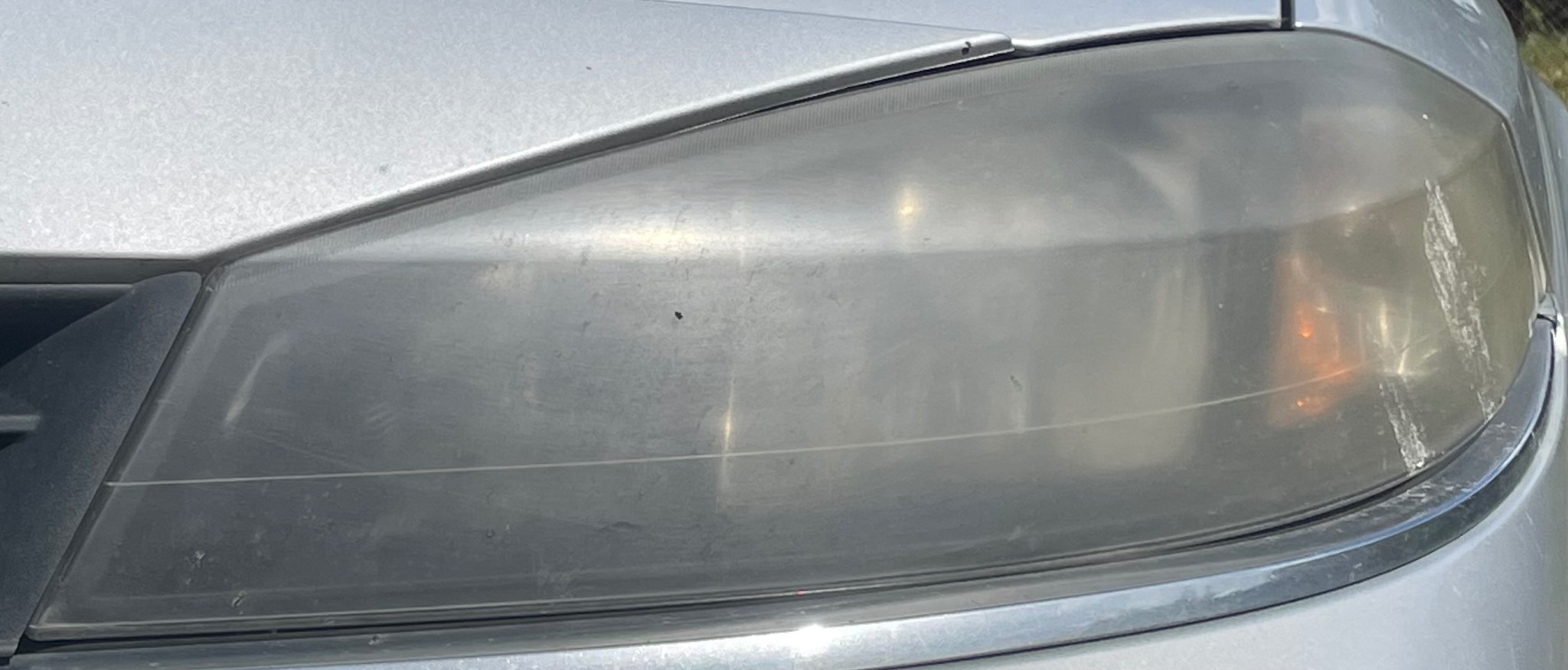 Prawy reflektor samochodu przed czyszczeniem, z widocznymi zarysowaniami i matową powierzchnią.