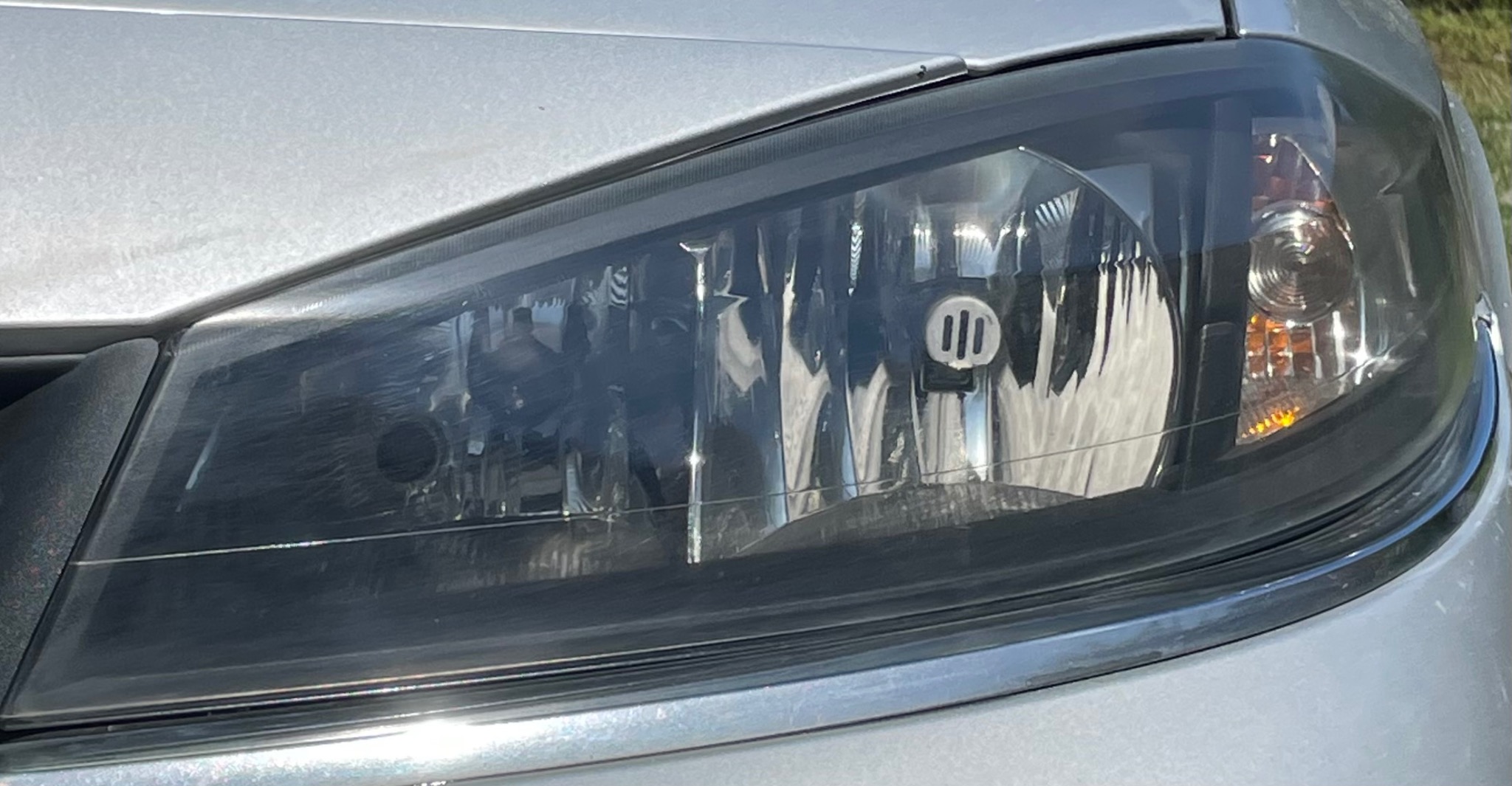 Reflektor samochodowy przed czyszczeniem z widocznymi smugami i zabrudzeniami, srebrny lakier karoserii.