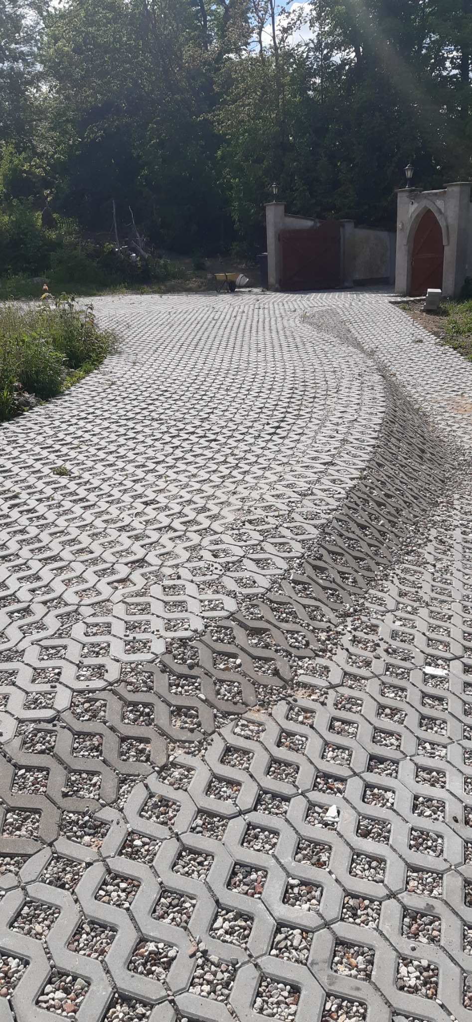 Ułożona ażurowa nawierzchnia z kostki betonowej wypełniona drobnym kruszywem na podjeździe prowadzącym do bramy wjazdowej.
