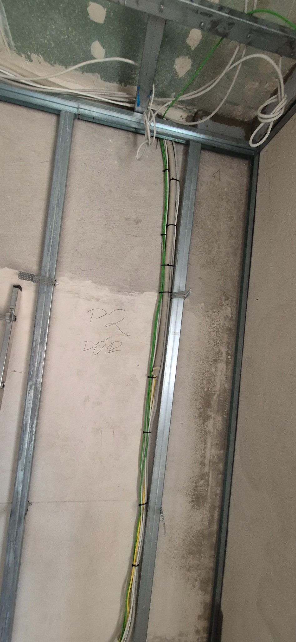 Stelaż z profili stalowych pod płytę karton-gips, widoczne przewody elektryczne zamocowane do profilu, ściana z napisem ołówkiem.