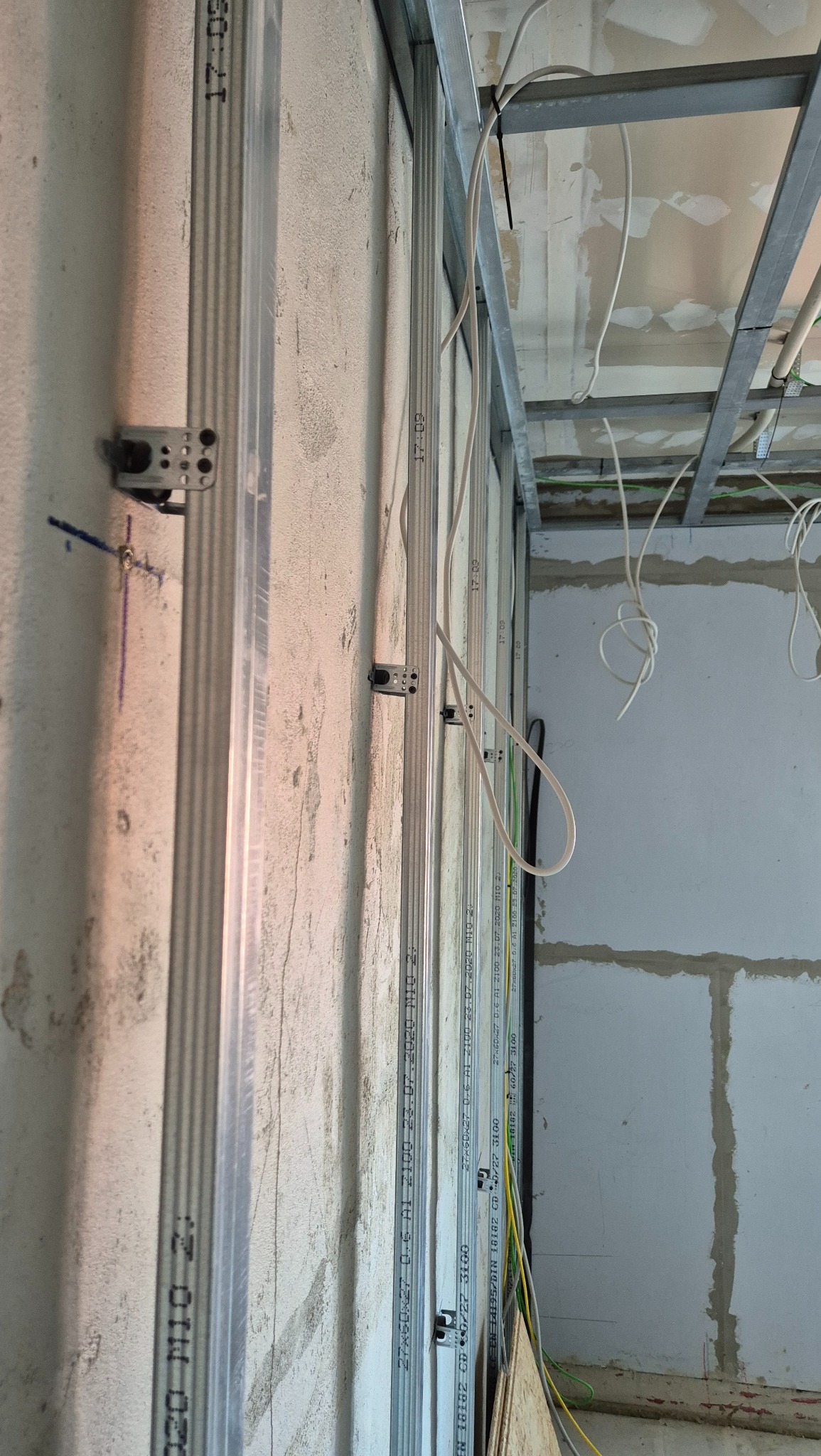 Montaż profili metalowych do ściany z bloczków, widoczne przewody elektryczne, konstrukcja sufitu podwieszanego w tle.