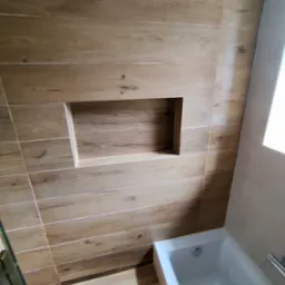 Wykończona łazienka z wanną i wnęką w ścianie wyłożonej płytkami imitującymi drewno.