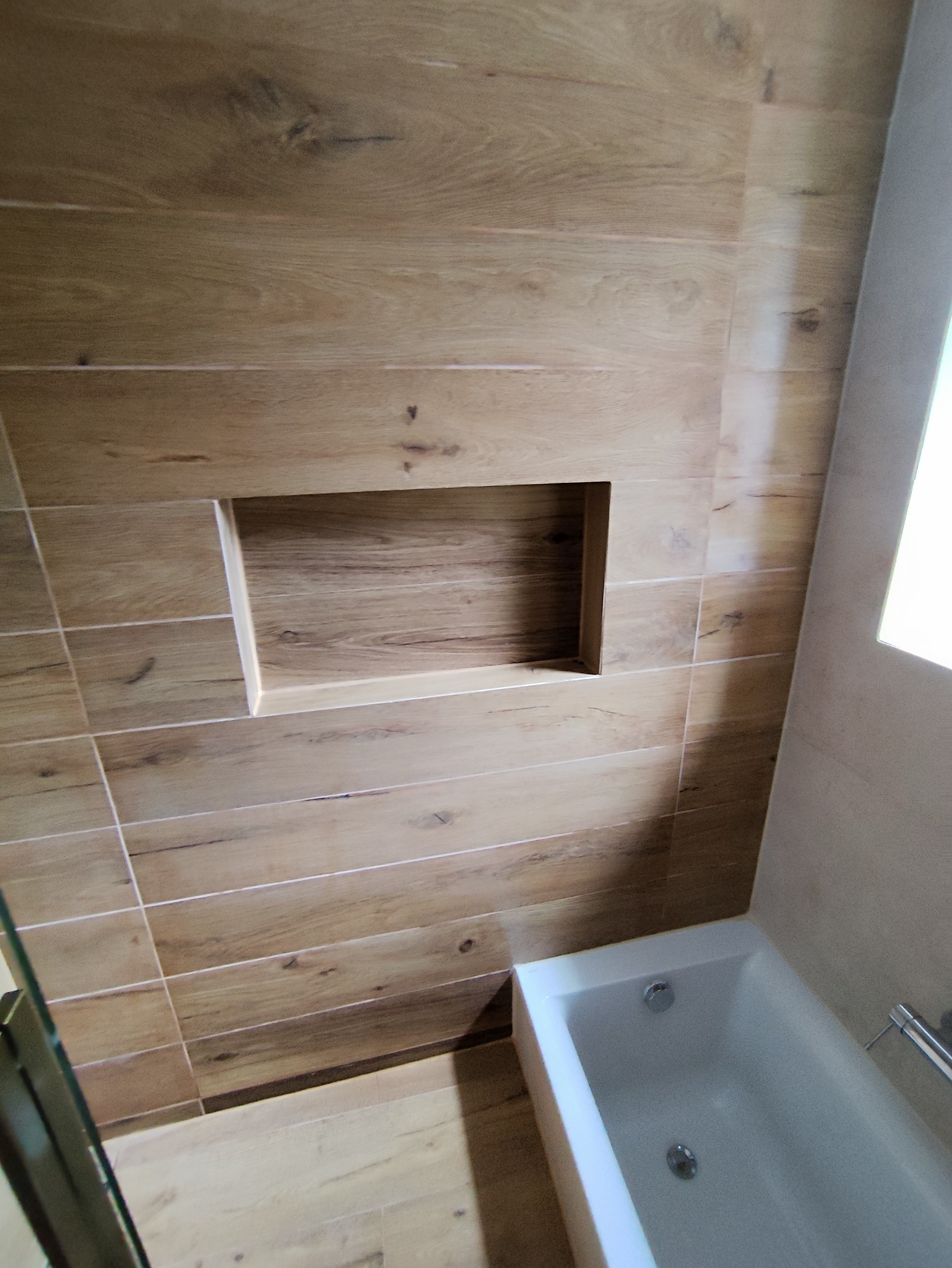 Wykończona łazienka z wanną i wnęką w ścianie wyłożonej płytkami imitującymi drewno.