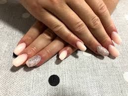 Dłonie z owalnymi paznokciami, część pomalowana na jasny róż, a część pokryta brokatowym lakierem, na tle w kropki.