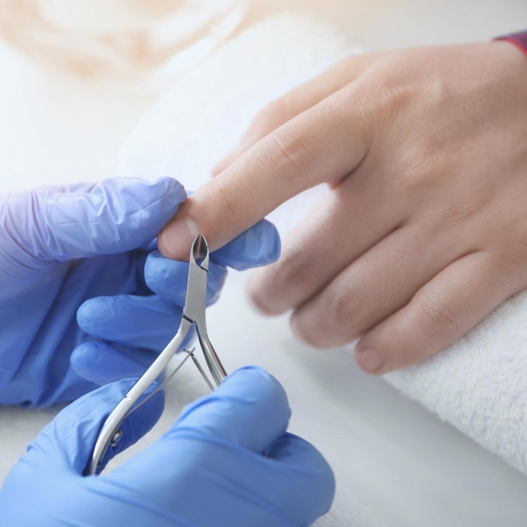 Przycięcie skórek przy paznokciu za pomocą cążek przez osobę w niebieskich rękawiczkach, na białym ręczniku.