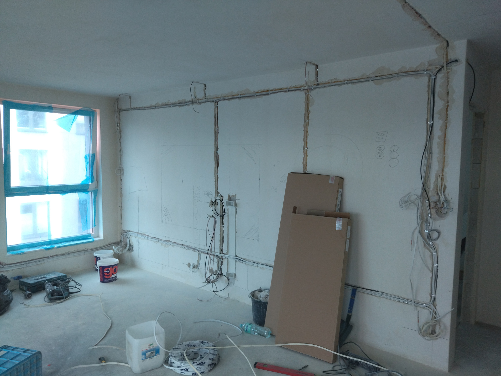 Nowa instalacja elektryczna w surowym wnętrzu: przewody w listwach na ścianach, puszki i kable zwisające, przygotowane do dalszych prac wykończeniowych.