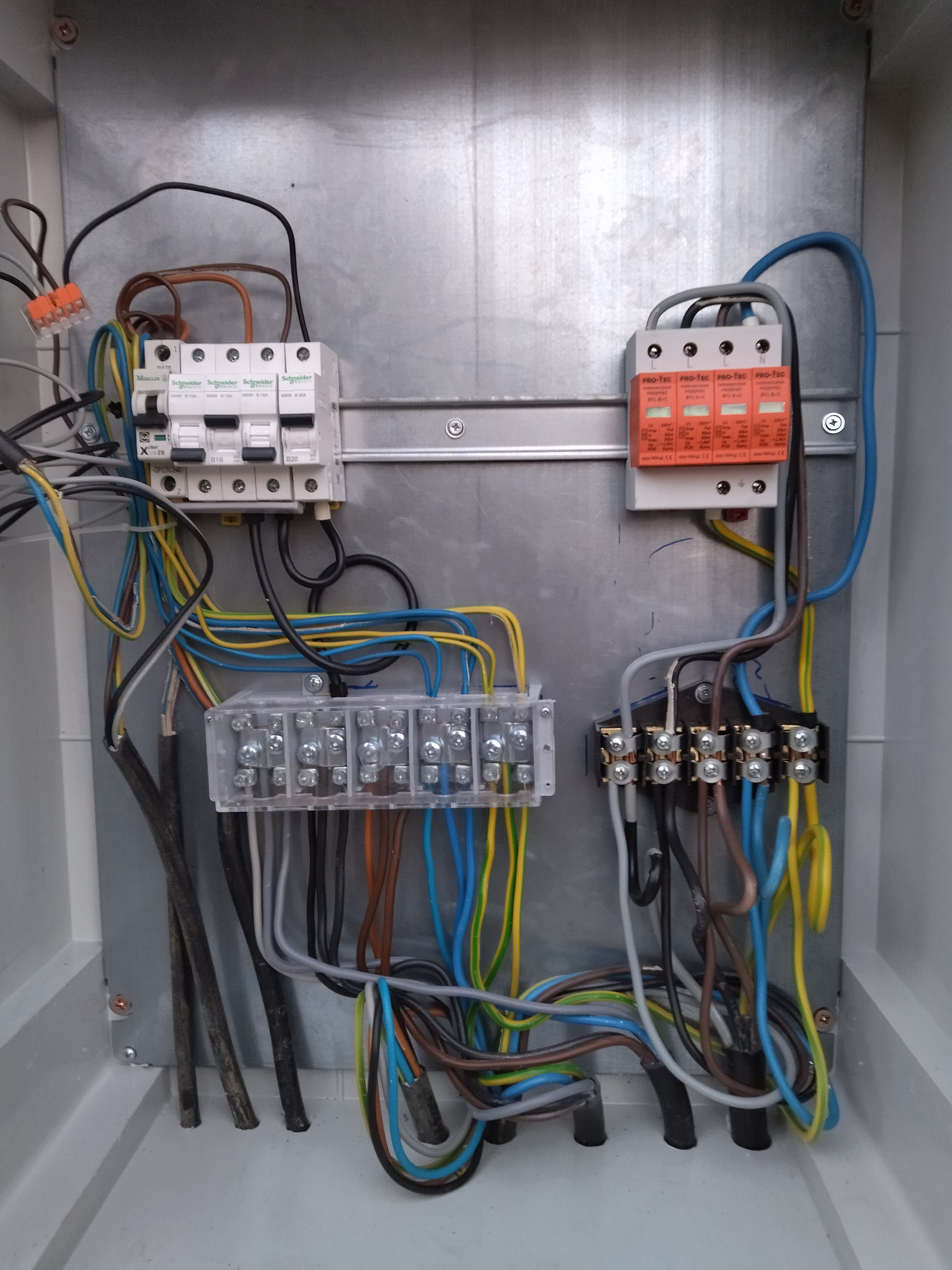 Wewnętrzny widok skrzynki elektrycznej z zamontowanymi bezpiecznikami, listwami zaciskowymi i przewodami o różnych kolorach, ułożonymi wewnątrz obudowy.