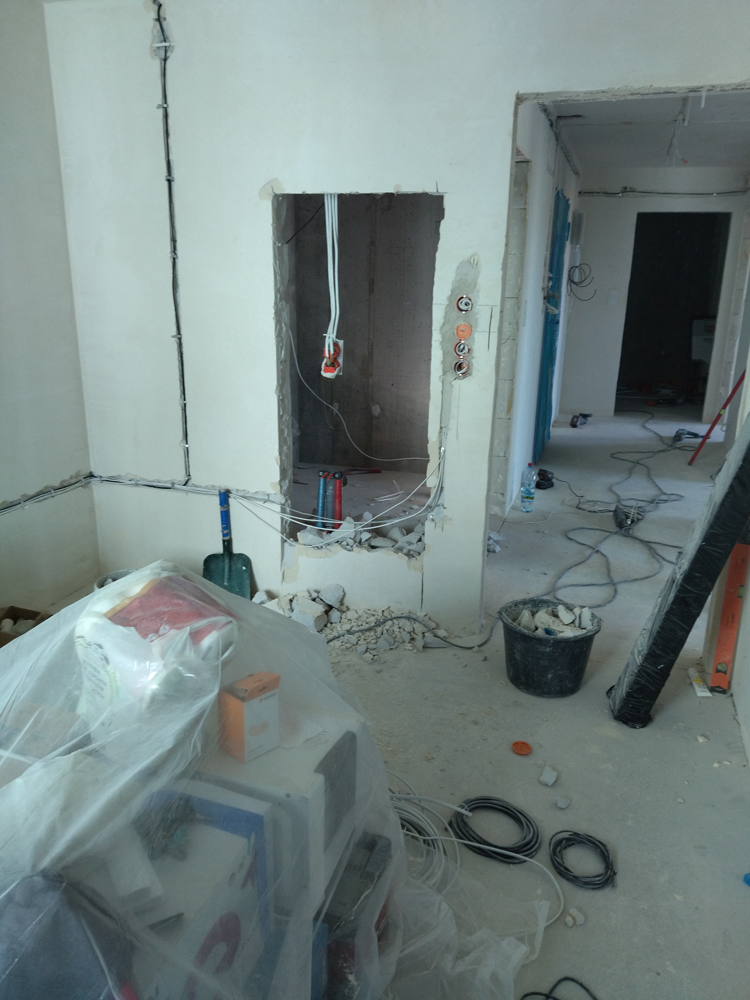 Wnętrze w trakcie prac remontowych: widoczne przewody elektryczne w ścianach, puszki instalacyjne, gruz i narzędzia. Etap przygotowania instalacji elektrycznej.