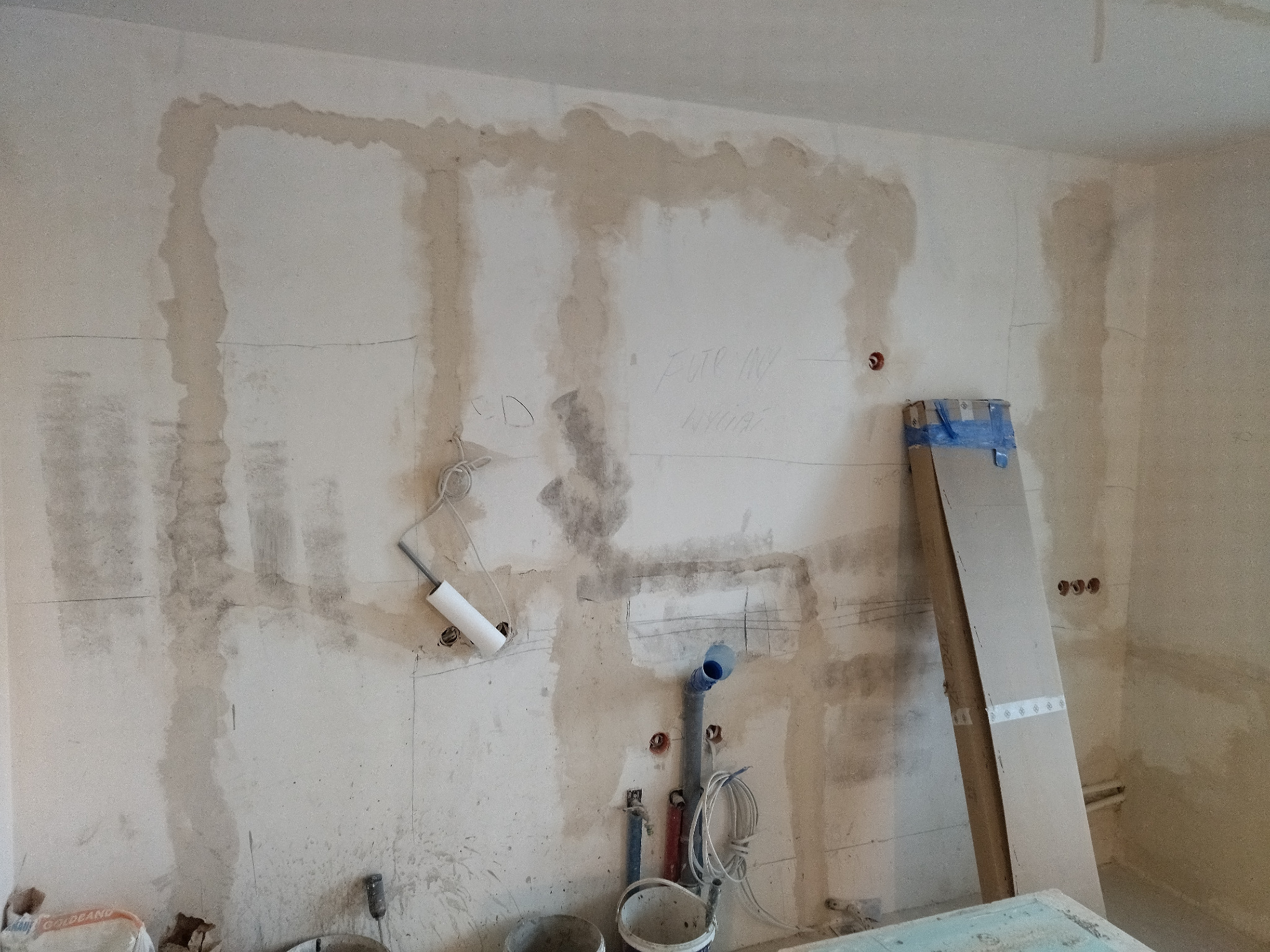 Ściana w trakcie remontu: widoczne instalacje wodne, elektryczne, ślady po kuciu, oznaczenia na ścianie i przygotowanie do dalszych prac wykończeniowych.