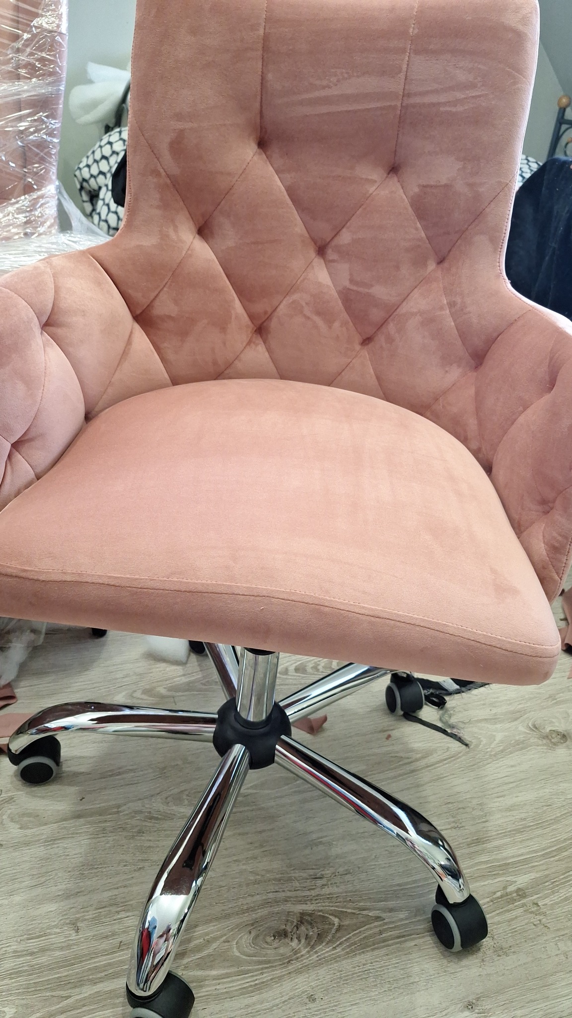 Różowe krzesło biurowe obrotowe z weluru, z pikowanym oparciem w romby i chromowaną podstawą na kółkach, widoczne z bliska na tle podłogi.