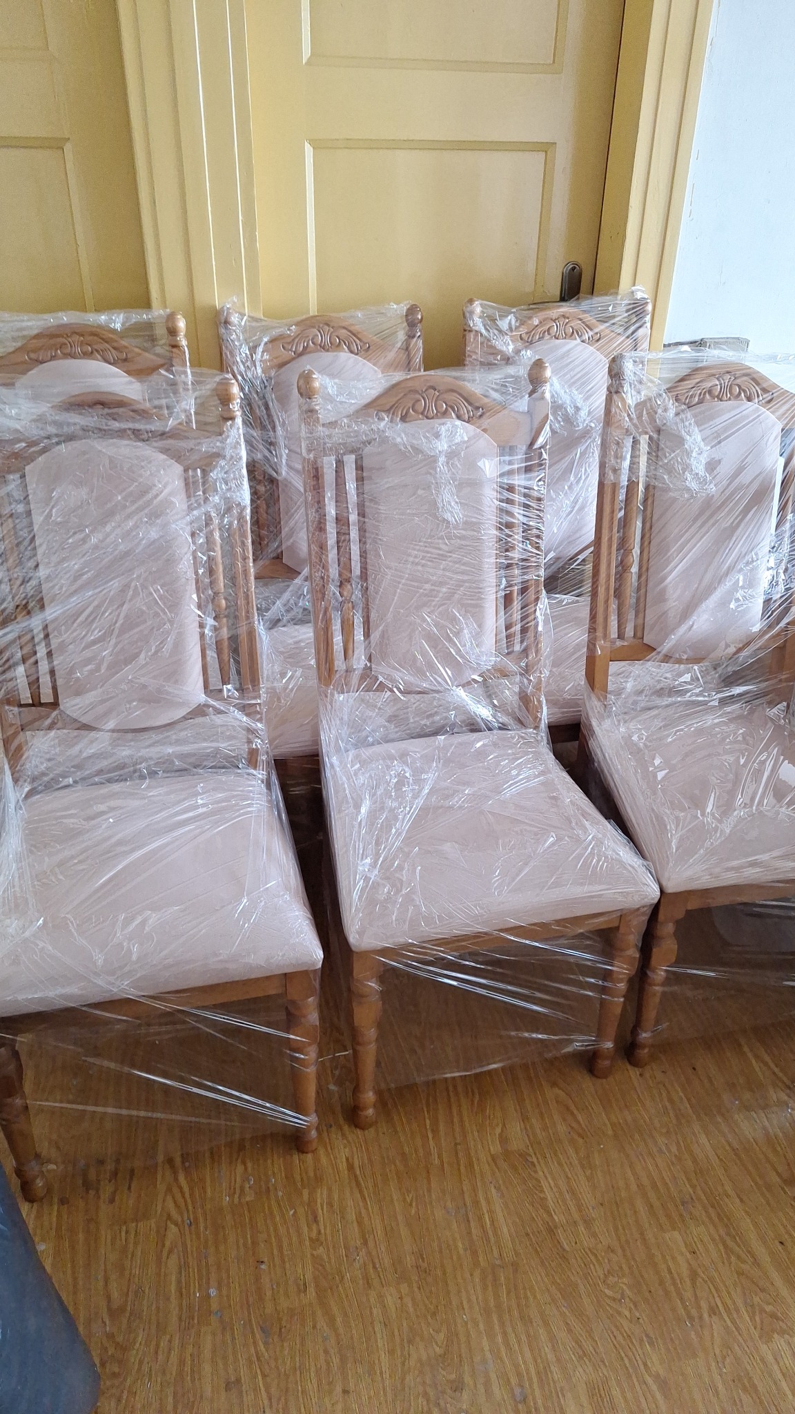 Rząd krzeseł z jasną tapicerką, zabezpieczonych folią stretch, ustawionych na drewnianej podłodze