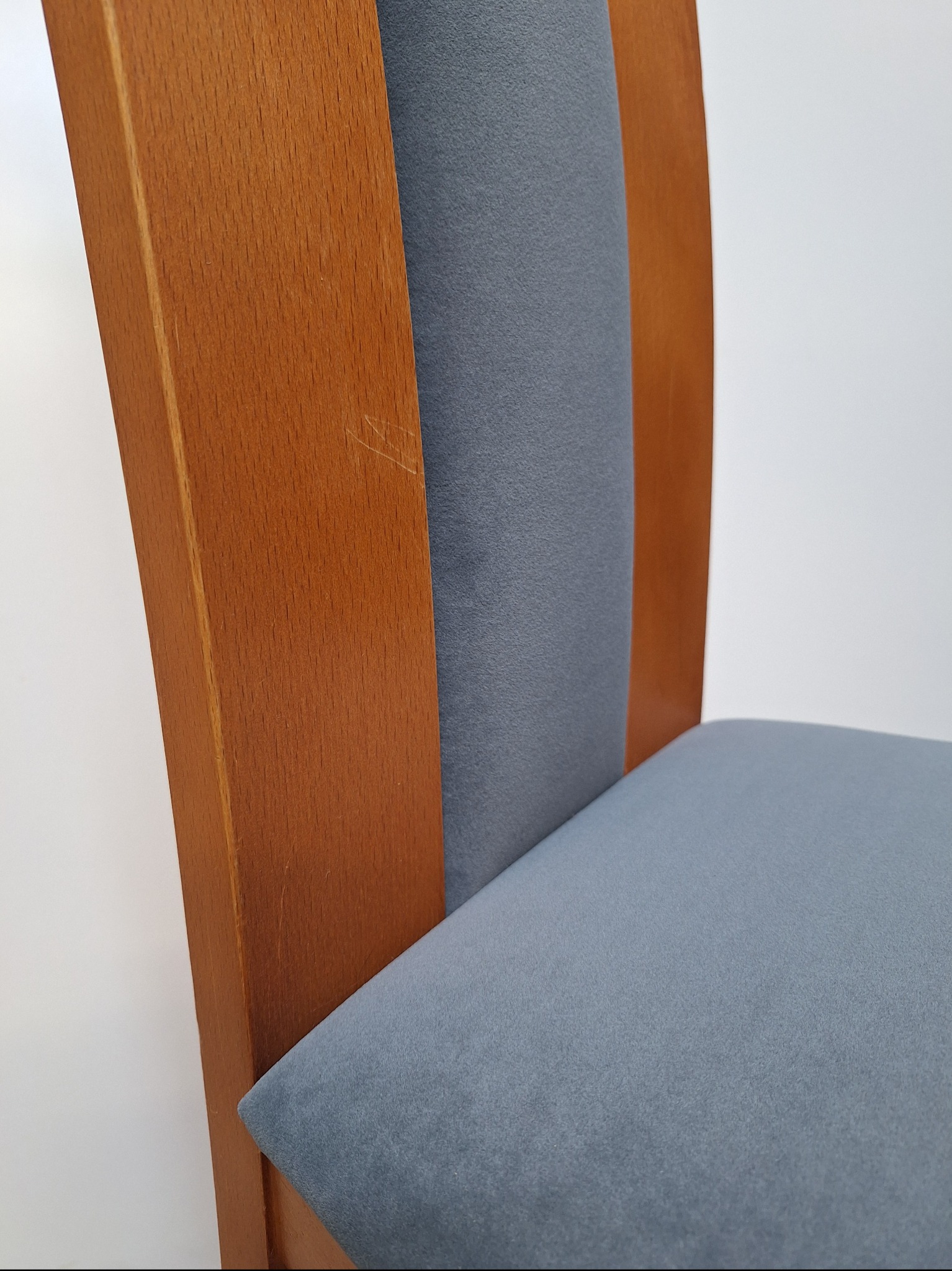 Fragment krzesła z drewnianym oparciem zarysowanym w górnej części i szarym tapicerowanym siedziskiem oraz oparciem.