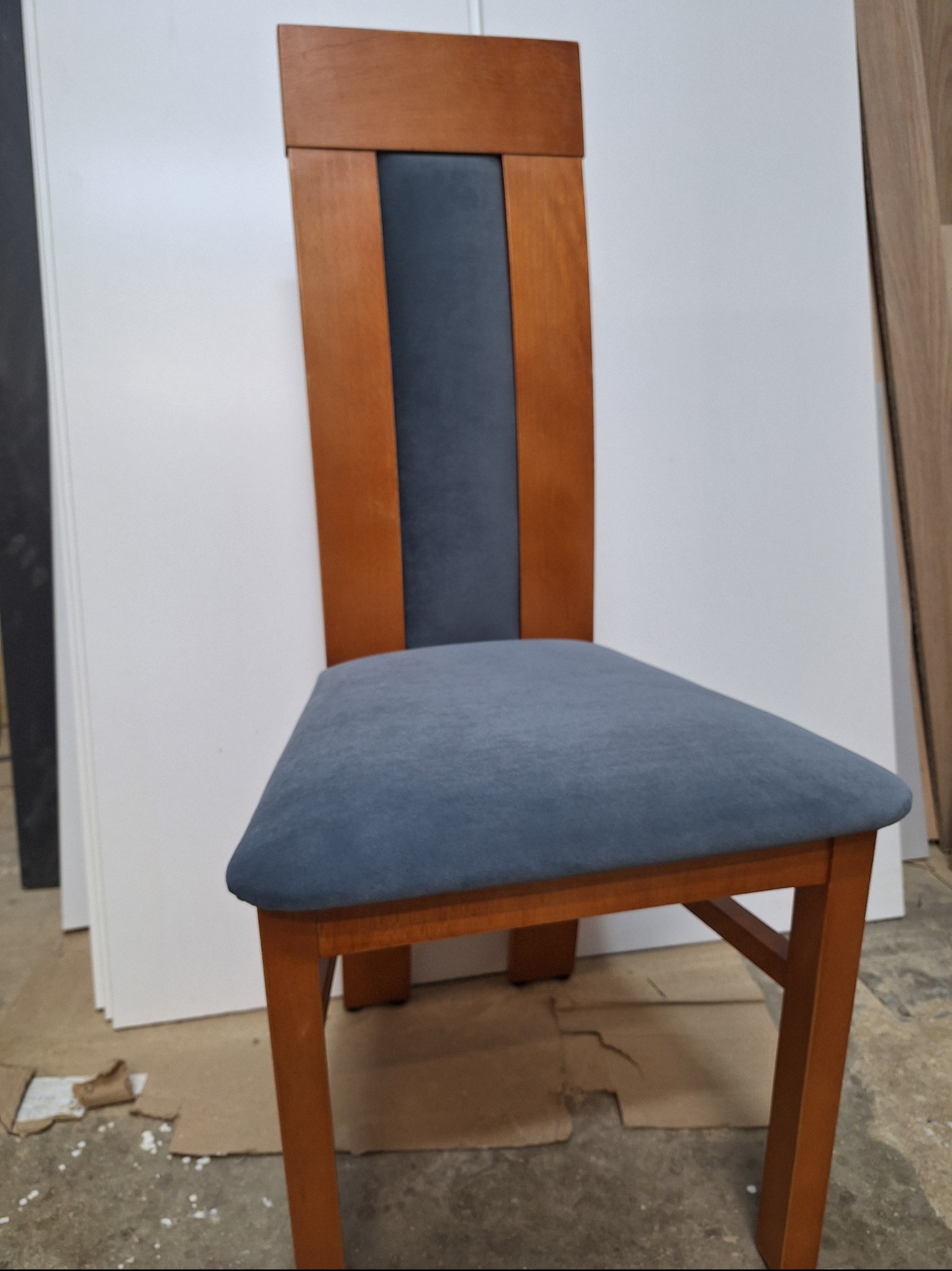 Krzesło tapicerowane w odcieniach brązu i szarości, z widocznym fragmentem białej ściany i podłogi z kartonami