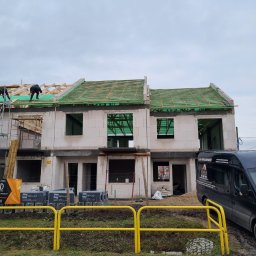 DAW- BUD - Budowa bliźniaka w stanie surowym otwartym, widoczne rusztowania, ekipa montująca konstrukcję dachu oraz zaparkowany bus firmy budowlanej.