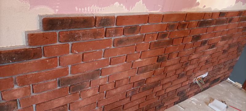 Ściana z czerwonej cegły dekoracyjnej w trakcie montażu w Krakowie, widoczne kable elektryczne wystające ze ściany i niedokończona górna krawędź.