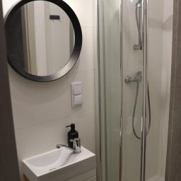 Oleksandr Zaremba Remonty - Nowoczesna, mała łazienka z kabiną prysznicową, okrągłym lustrem z czarną ramą, białą umywalką z szafką i czarnym dozownikiem mydła w płynie.