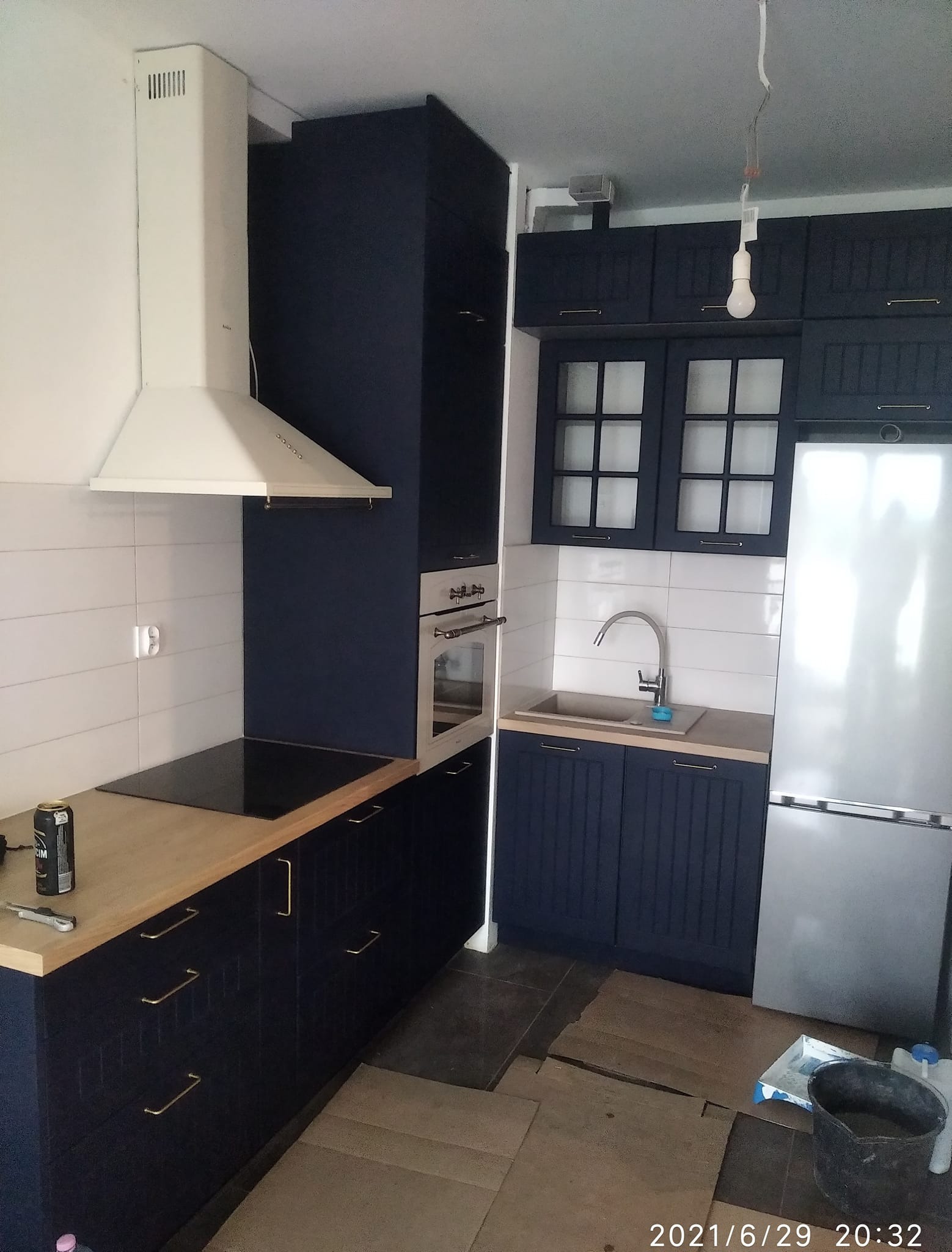 Granatowa zabudowa kuchenna z drewnianymi blatami, białymi płytkami i srebrną lodówką; widoczna puszka napoju energetycznego na blacie.