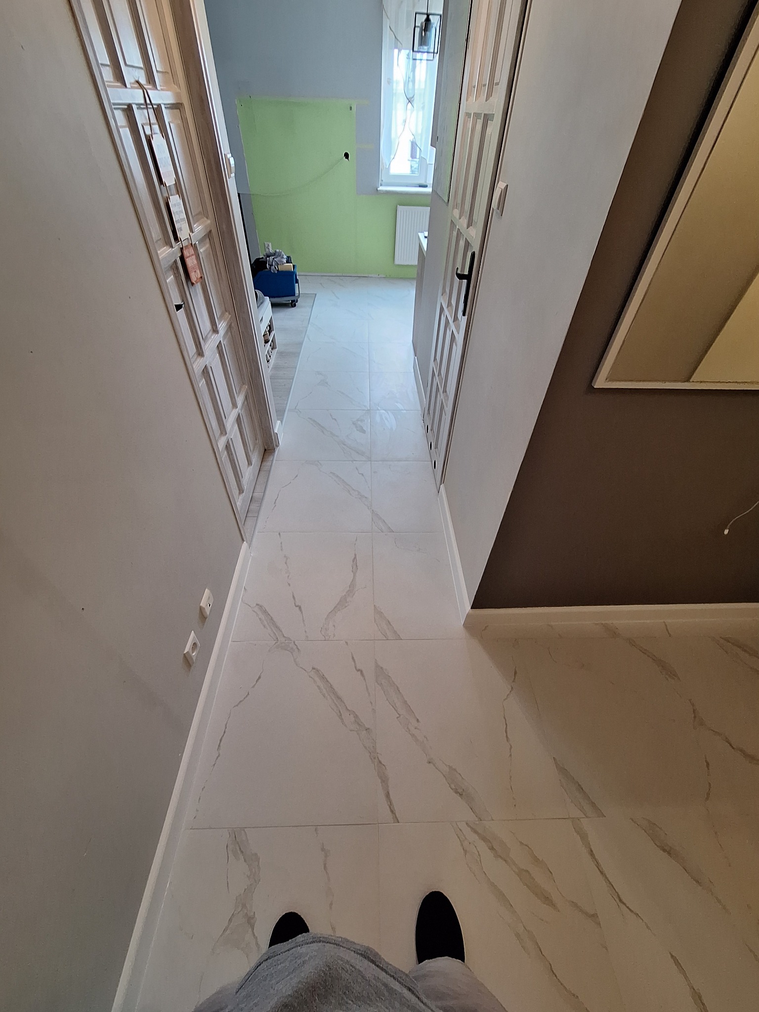 Korytarz z nową białą podłogą z marmurowym wzorem, świeżo pomalowane ściany i odnowione drzwi.