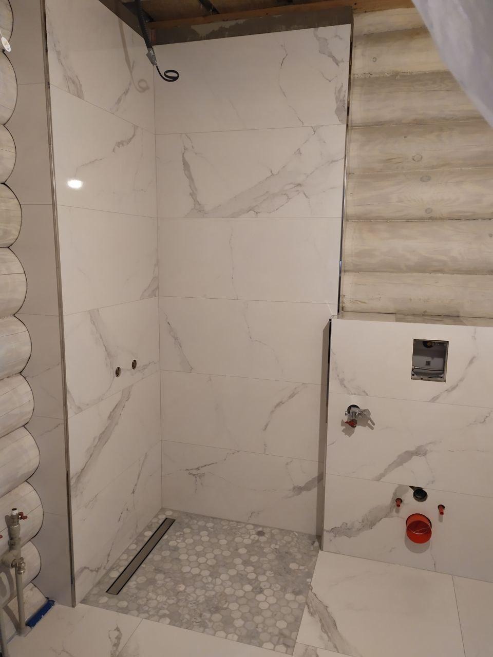 Wnętrze łazienki w trakcie prac, z marmurkowymi płytkami na ścianach, heksagonalną mozaiką na podłodze prysznica i widocznymi elementami instalacji wodnej.
