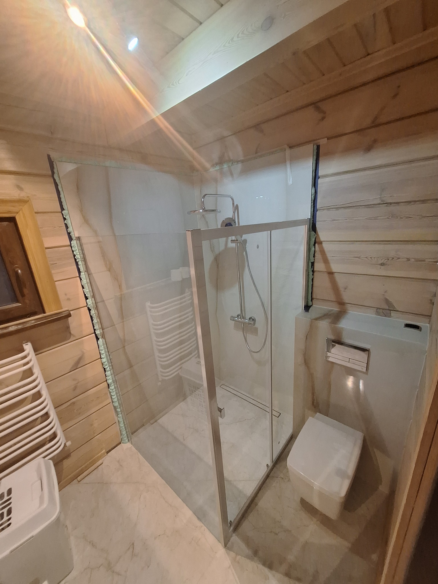 Wykończona łazienka w drewnie z kabiną prysznicową ze szklaną ścianką, wiszącą toaletą i grzejnikiem drabinkowym.