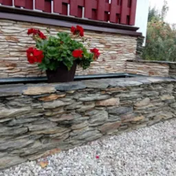 Kamienny murek z kwiatami w donicy, wykonany z nieregularnych płat&oacute;w kamienia, otoczony białym żwirem.