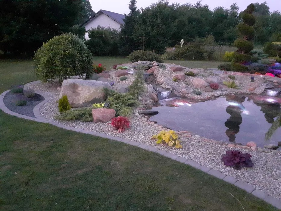 Ogród z oczkiem wodnym, kaskadą, podświetleniem i ozdobnymi kamieniami oraz roślinami, obrzeże z kostki.