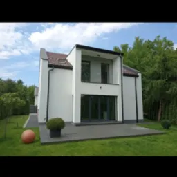 Nowoczesny dom z białą elewacją, widok z zewnątrz, z przesuwnymi drzwiami tarasowymi, szarym tarasem i kulistą dekoracją ogrodową na trawniku.