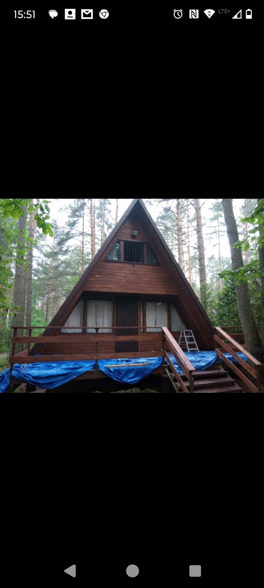 Dom w kształcie litery A w lesie, z drewnianą elewacją w trakcie zabezpieczania folią malarską przed pracami renowacyjnymi.