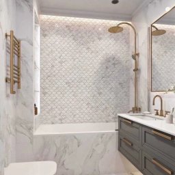Maxxxbud - Elegancka łazienka z marmurowymi płytkami, mozaiką w kształcie rybiej łuski nad wanną i złotą armaturą. Szara szafka pod umywalką z subtelnym oświetleniem.