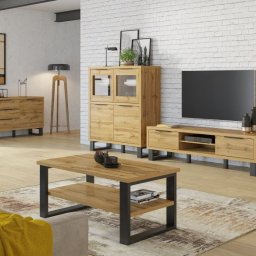 Zbyszek Molenda - Jasne, drewniane meble w salonie z ceglaną ścianą. Komoda, szafka RTV, witryna i stolik kawowy z czarnymi, metalowymi nogami. Nowoczesny design, ciepłe oświetlenie.