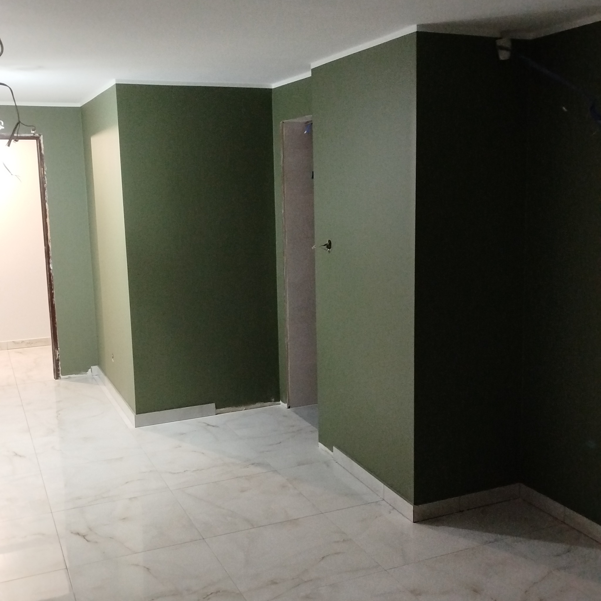 Pomieszczenie po malowaniu ścian na odcienie zieleni, z białymi listwami przypodłogowymi i marmurową podłogą. Widoczne fragmenty ościeżnic drzwiowych.