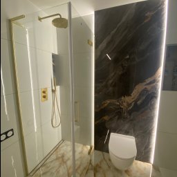 TILER PRO SERGII KUZOVINSKYI - Nowoczesna łazienka z kabiną prysznicową typu walk-in z złotymi detalami, marmurową ścianą z podświetleniem LED i podwieszaną toaletą.