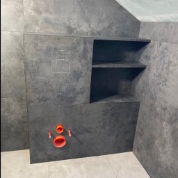 TILER PRO SERGII KUZOVINSKYI - Wykończona łazienka z szarymi płytkami imitującymi kamień, wnęką z półkami i instalacją podtynkową WC z pomarańczowymi elementami. Minimalistyczny design.