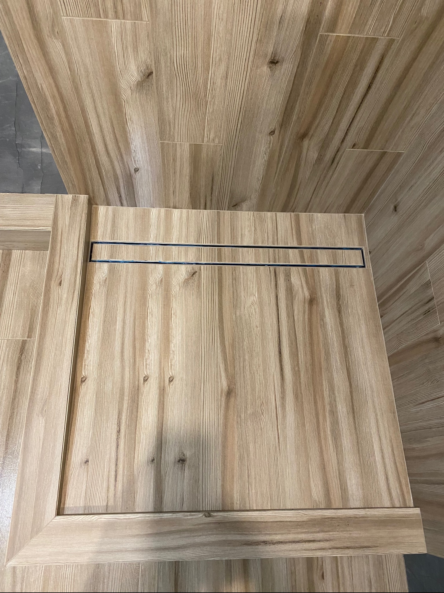 Wykończona kabina prysznicowa typu walk-in z odpływem liniowym, wyłożona płytkami imitującymi drewno, widok z góry.