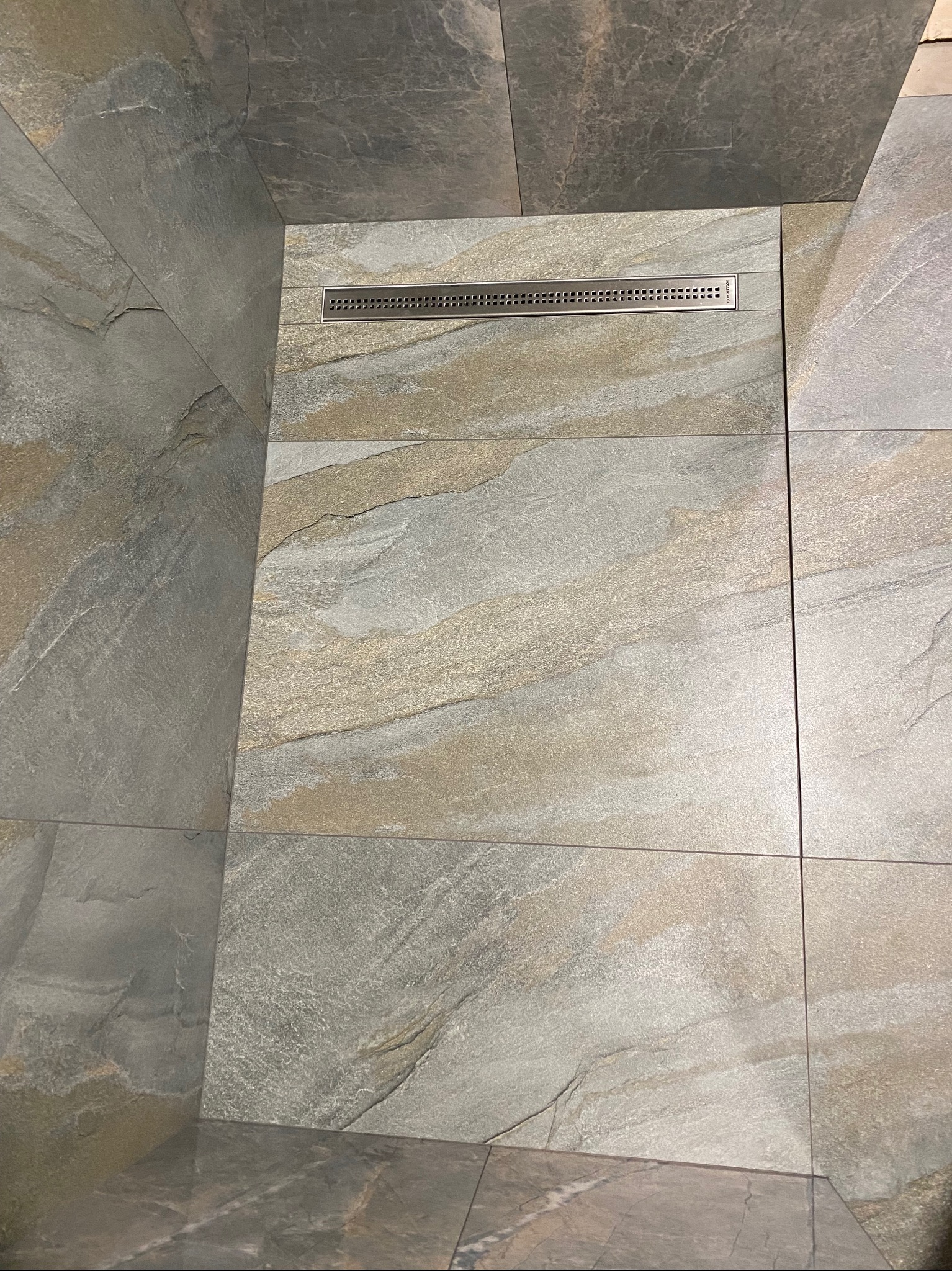 Płytki podłogowe i ścienne w łazience z odpływem liniowym, imitujące kamień naturalny w odcieniach szarości i beżu, ułożone z precyzją.