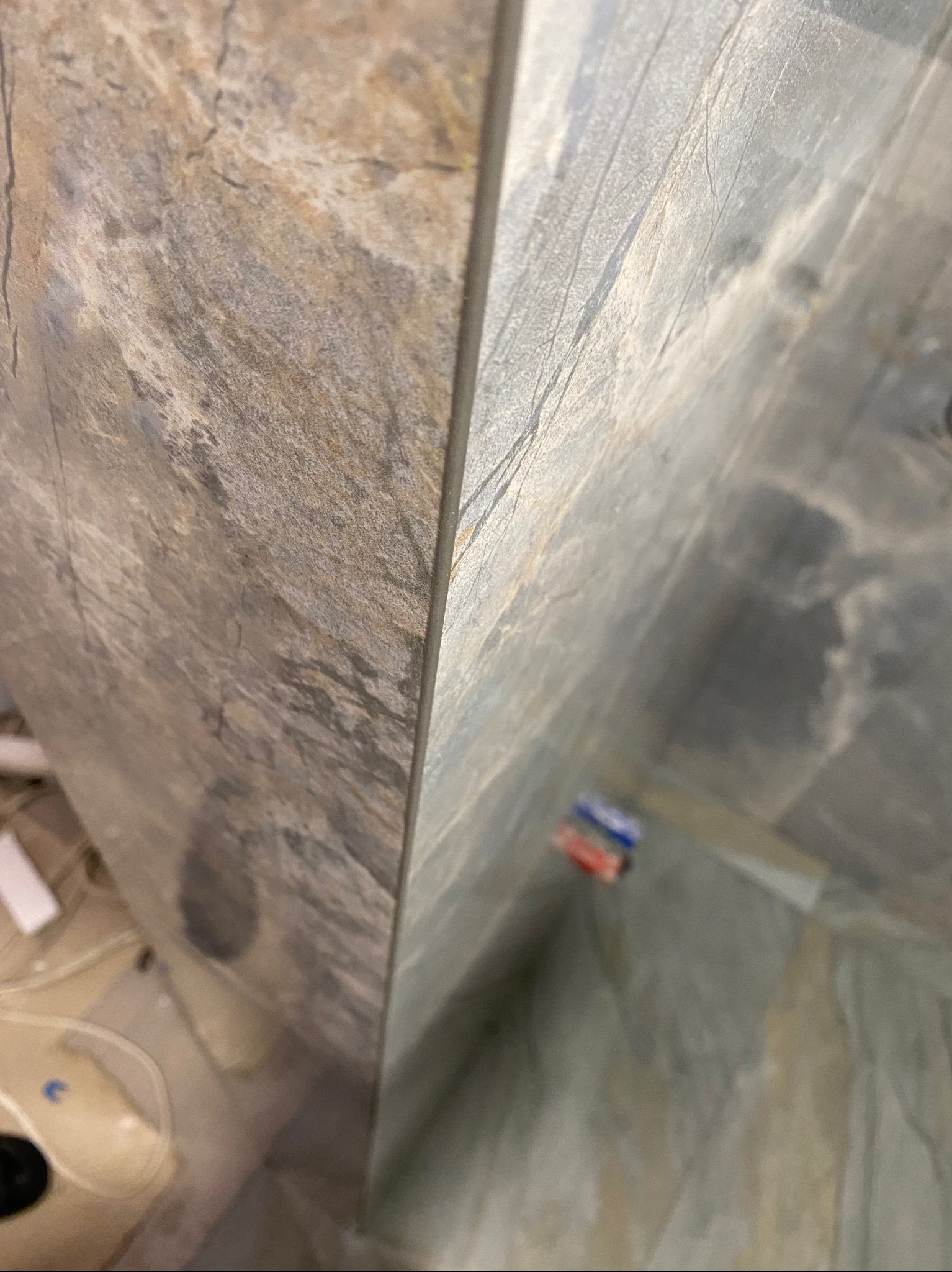 Ułożone płytki imitujące kamień na ścianie w łazience, widoczne kable i rurki instalacji wodnej w tle.