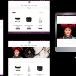 Prezentacja responsywnej strony internetowej Mayzam na monitorze, ukazująca sekcję 'About Me', produkty kosmetyczne oraz portret kobiety z kwiatami we włosach.