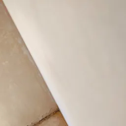 Fragment ściany po tynkowaniu maszynowym, widoczna gładka, jasna powierzchnia tynku oraz surowa podłoga z widocznymi pęknięciami i pozostałościami po pracach budowlanych.