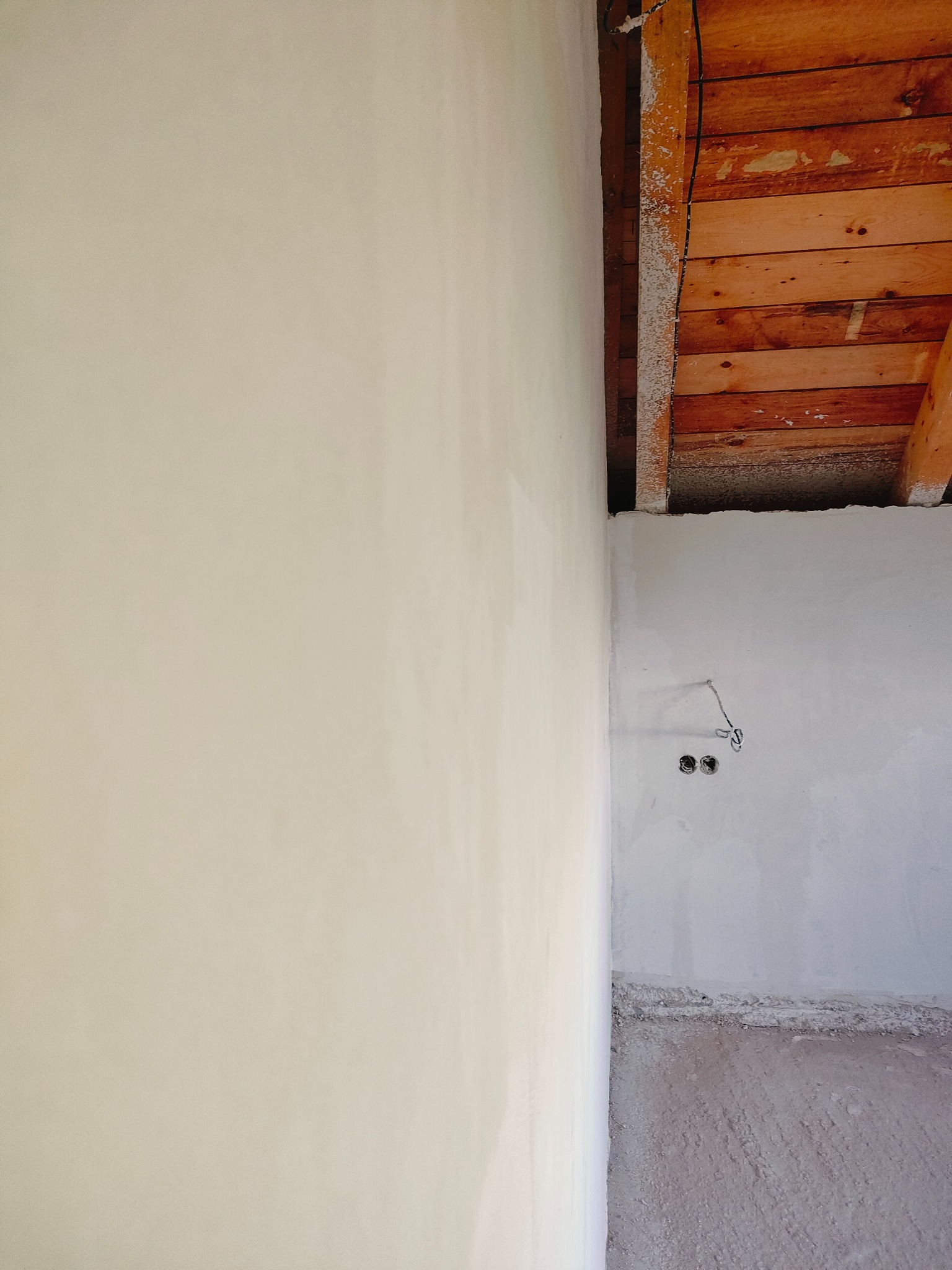 Gładka ściana po tynkowaniu maszynowym w Cieszynie, widoczne drewniane elementy stropu i przygotowane punkty elektryczne.