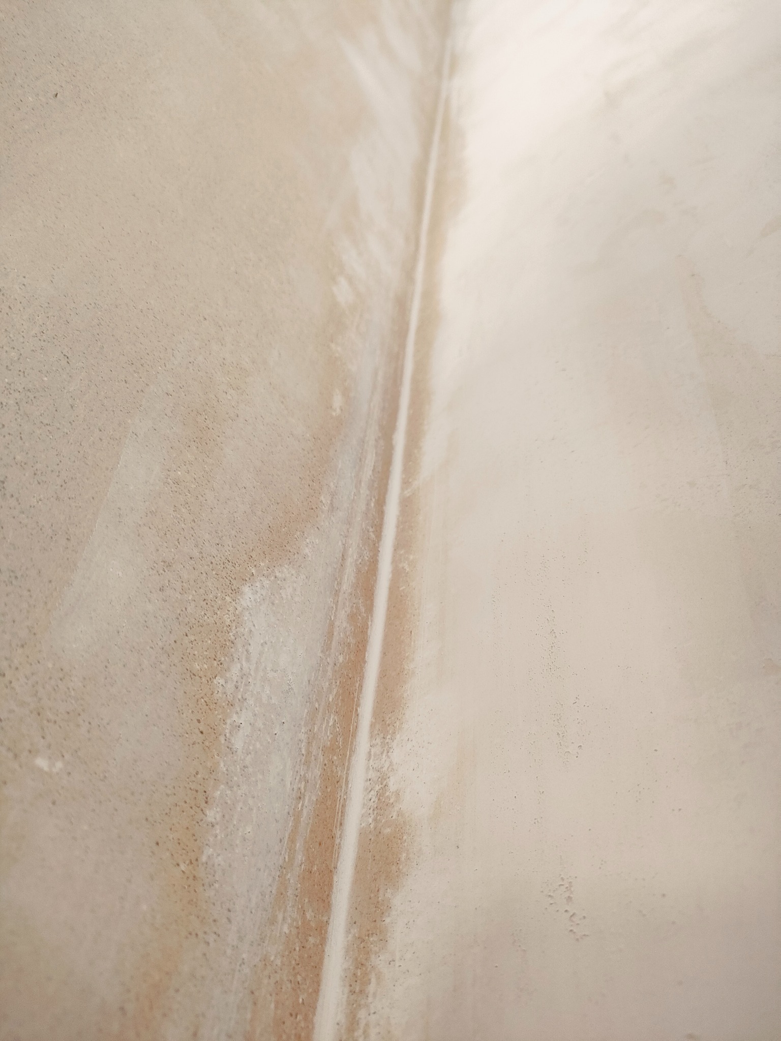 Świeżo nałożona, jasna warstwa tynku na styku dwóch ścian, widoczne niedoskonałości i zacieki.