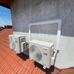 Bartłomiej Bombik - Dwa klimatyzatory Sinclair zamontowane na dachu z czerwonej dachówki, zabezpieczone białą ramą ochronną na elewacji budynku.