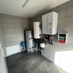 Bartłomiej Bombik - Pomieszczenie techniczne z zainstalowanym systemem grzewczym: zbiornik akumulacyjny Joule, zasobnik CWU, pompa ciepła Ecodan Mitsubishi Electric oraz skrzynka elektryczna z gniazdami siłowymi.