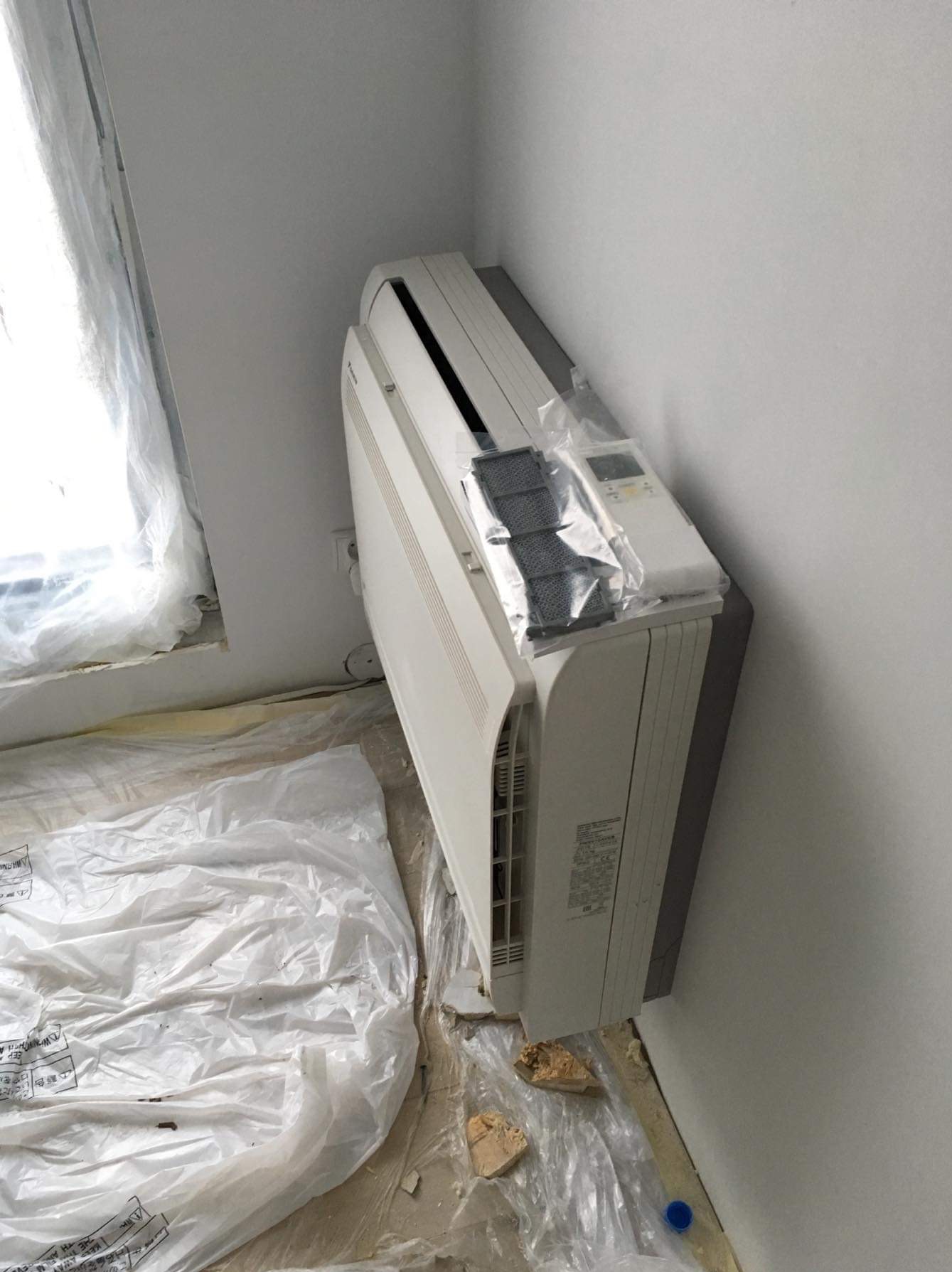 Wnętrze w trakcie montażu klimatyzacji: biały klimatyzator ścienny, zabezpieczona folią podłoga, widoczne filtry i pilot w folii ochronnej.