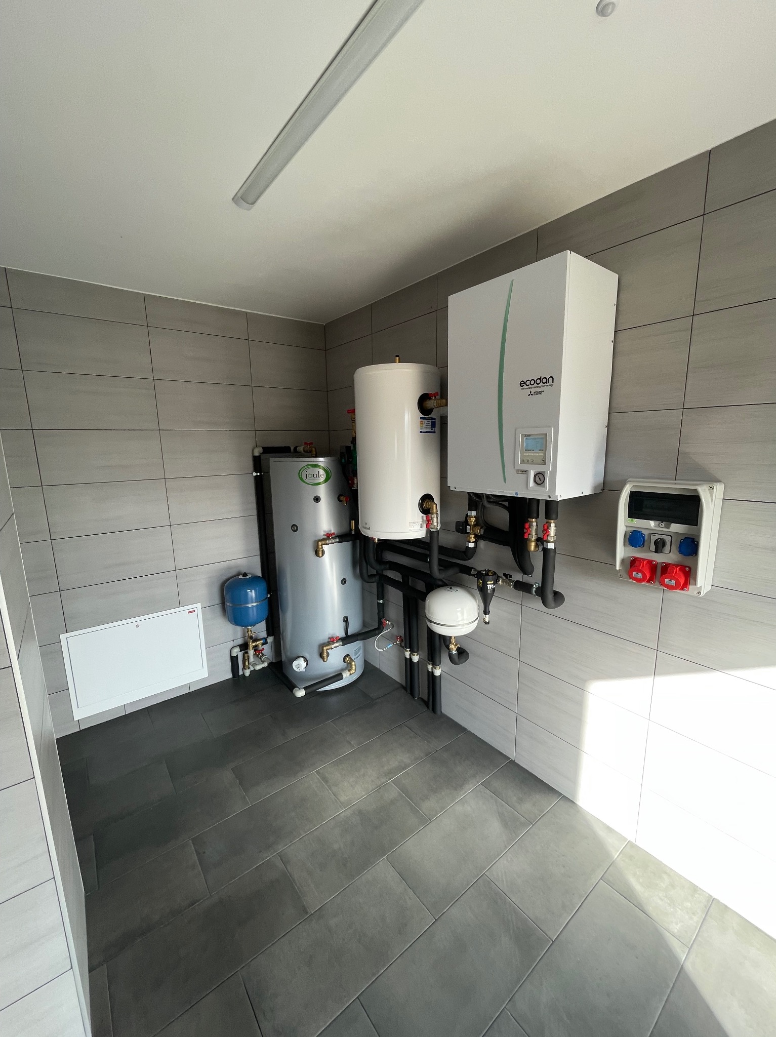 Pomieszczenie techniczne z zainstalowanym systemem grzewczym: zbiornik akumulacyjny Joule, zasobnik CWU, pompa ciepła Ecodan Mitsubishi Electric oraz skrzynka elektryczna z gniazdami siłowymi.