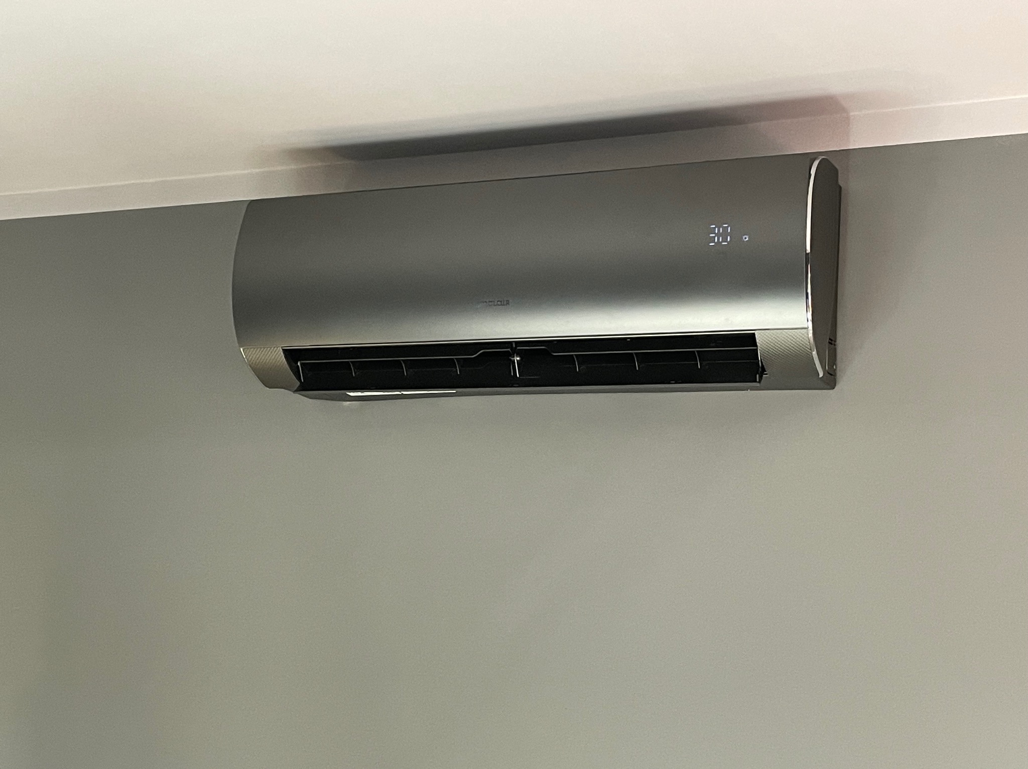 Zamontowany na ścianie, szary klimatyzator z wyświetlaczem pokazującym temperaturę 30 stopni Celsjusza.