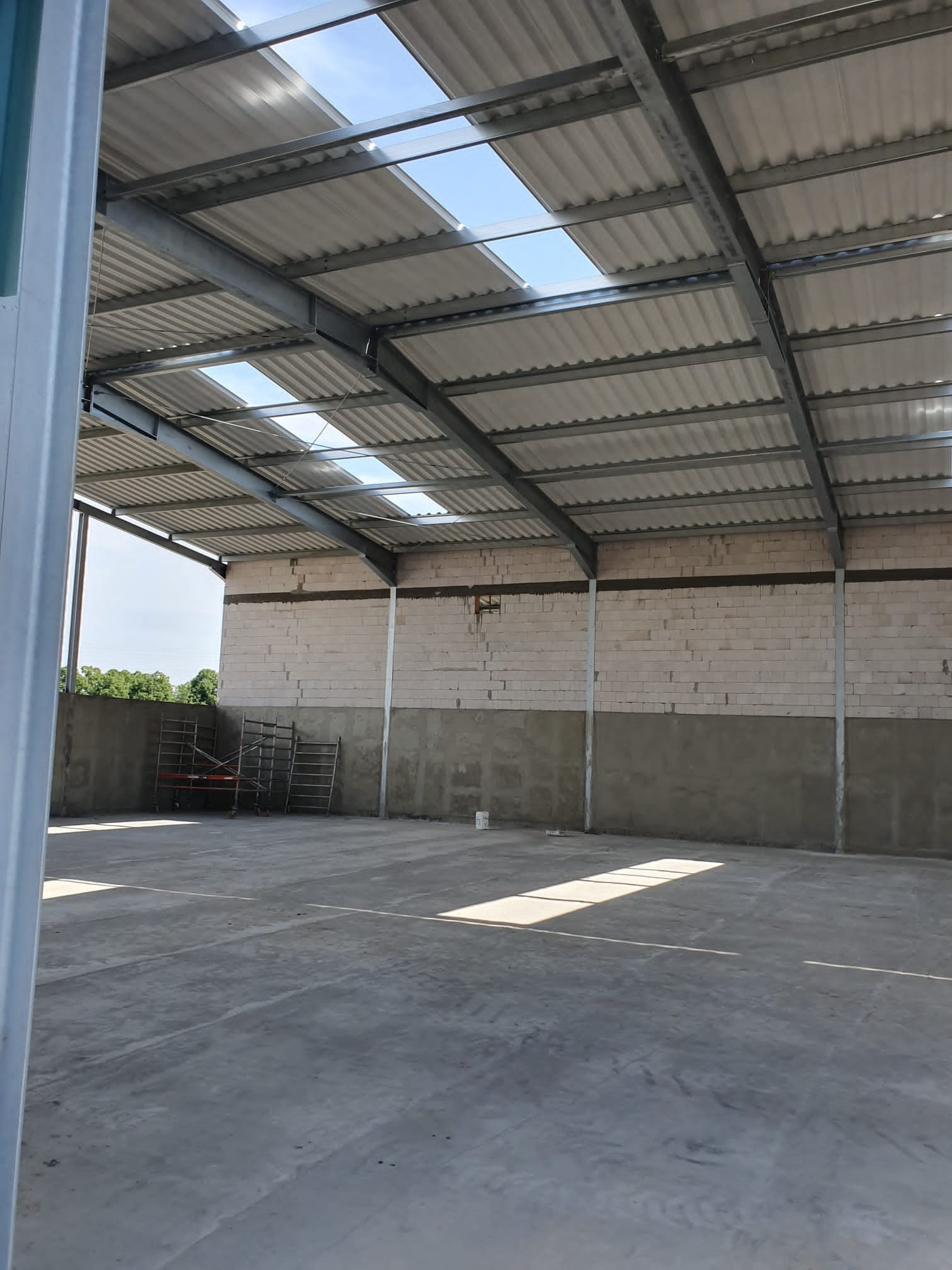 Wnętrze hali w stanie surowym: betonowa posadzka, ściany z betonu i bloczków, stalowa konstrukcja dachu z świetlikami.
