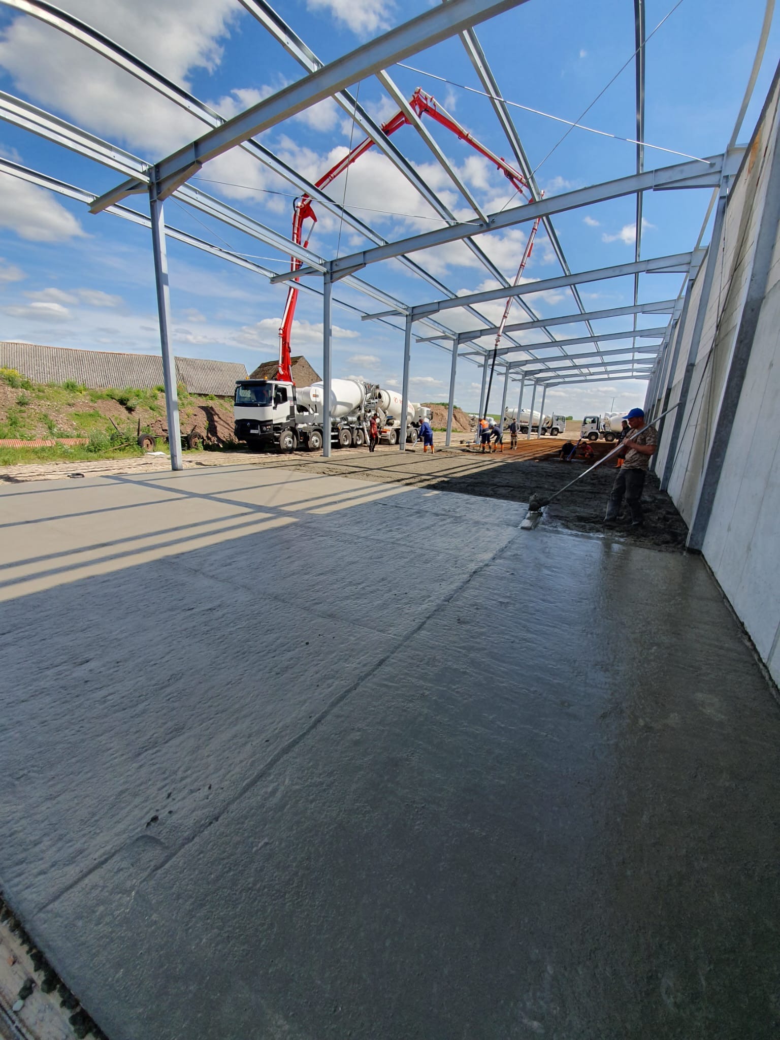 Wnętrze konstrukcji stalowej z betonową wylewką w trakcie realizacji; pracownicy wyrównują powierzchnię, w tle betoniarka z pompą do betonu.