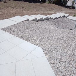 Dominik Kunda - Wykończone schody z kostki brukowej i kamiennego grysu na nierównym terenie ogrodu.