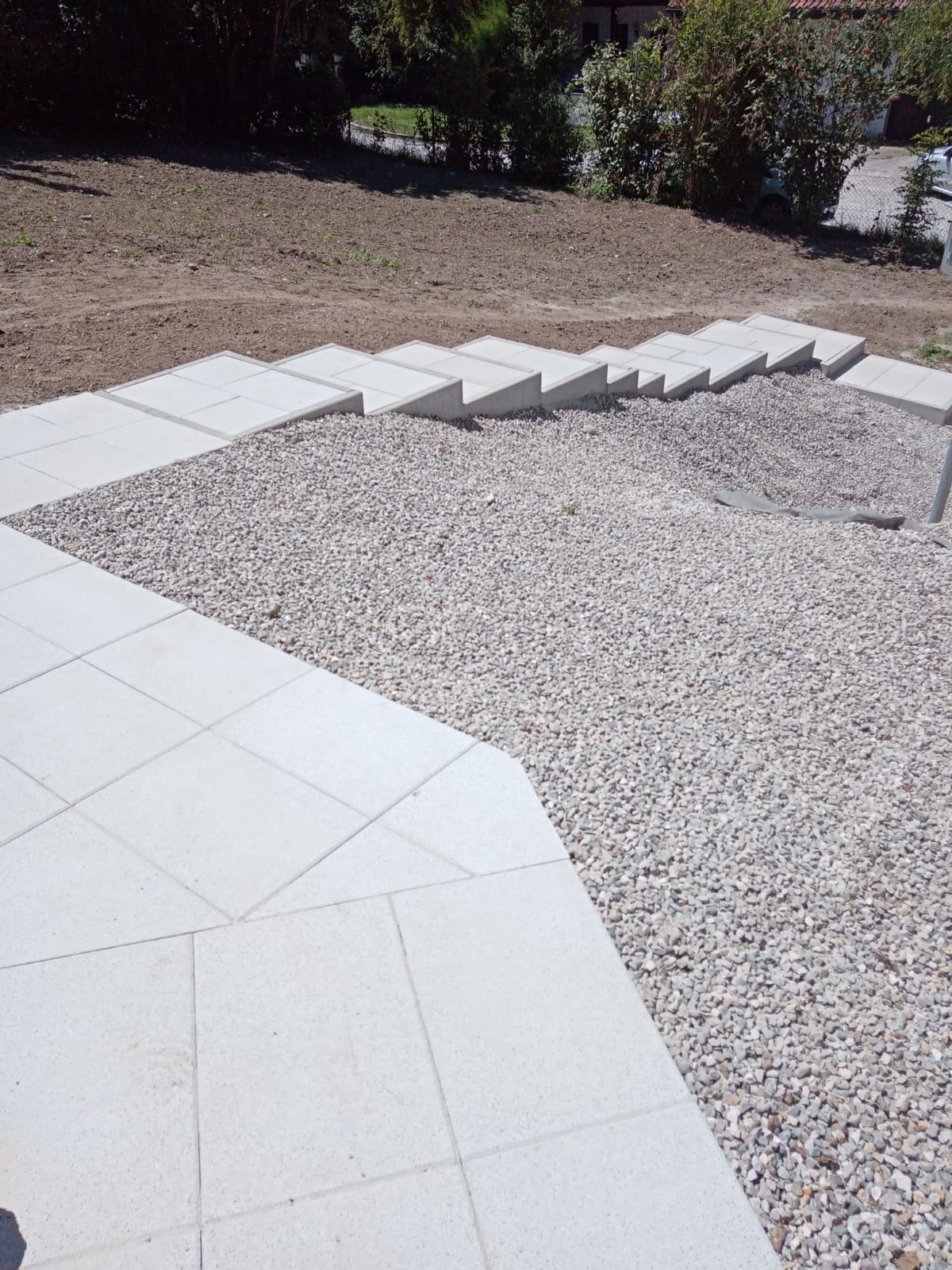 Wykończone schody z kostki brukowej i kamiennego grysu na nierównym terenie ogrodu.