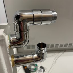 Aleksander Musioł - Błyszczące chromowane rury łączące grzejnik, widoczna taśma uszczelniająca i narzędzia na marmurowym blacie.